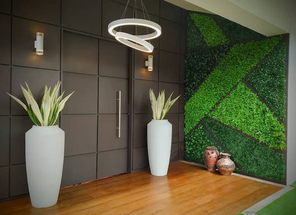 Jardín vertical con diseño geométrico en la entrada de una vivienda, junto a jarrones de barro
